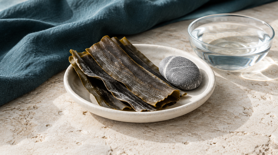 Alghe kombu essiccate in una ciotola chiara, pietra levigata e acqua su una superficie di calcare.